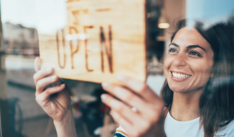 Smiling business owner placing an “Open” sign on a storefront window.